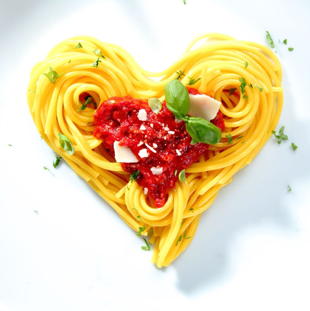Spaghetti with tomato and cheese sauce garnished with basil arranged in coils into a heart shape for love,